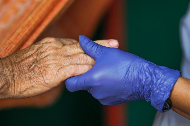 Mano con guante de látex azul tomando la mano de una persona de la tercera edad